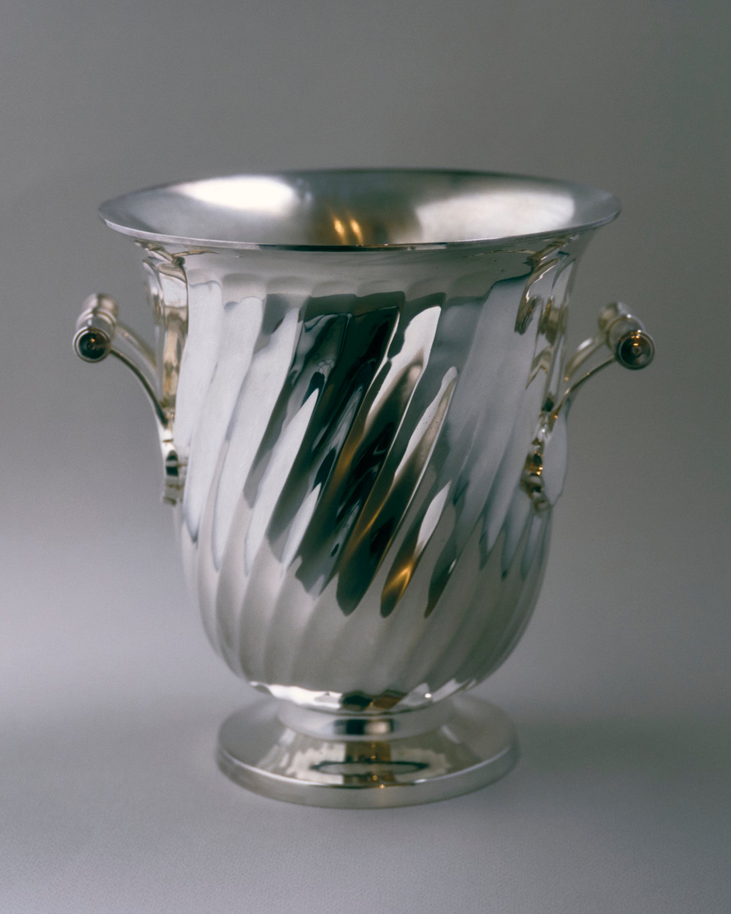 Seau à champagne en métal argenté, à panse galbée ornée de cannelures torsadées et reposant sur un piédouche circulaire. Poignées latérales à barres tournées et extrémités sphériques. Travail européen des années 1950.
Très bel état, légère patine conforme à l'âge.