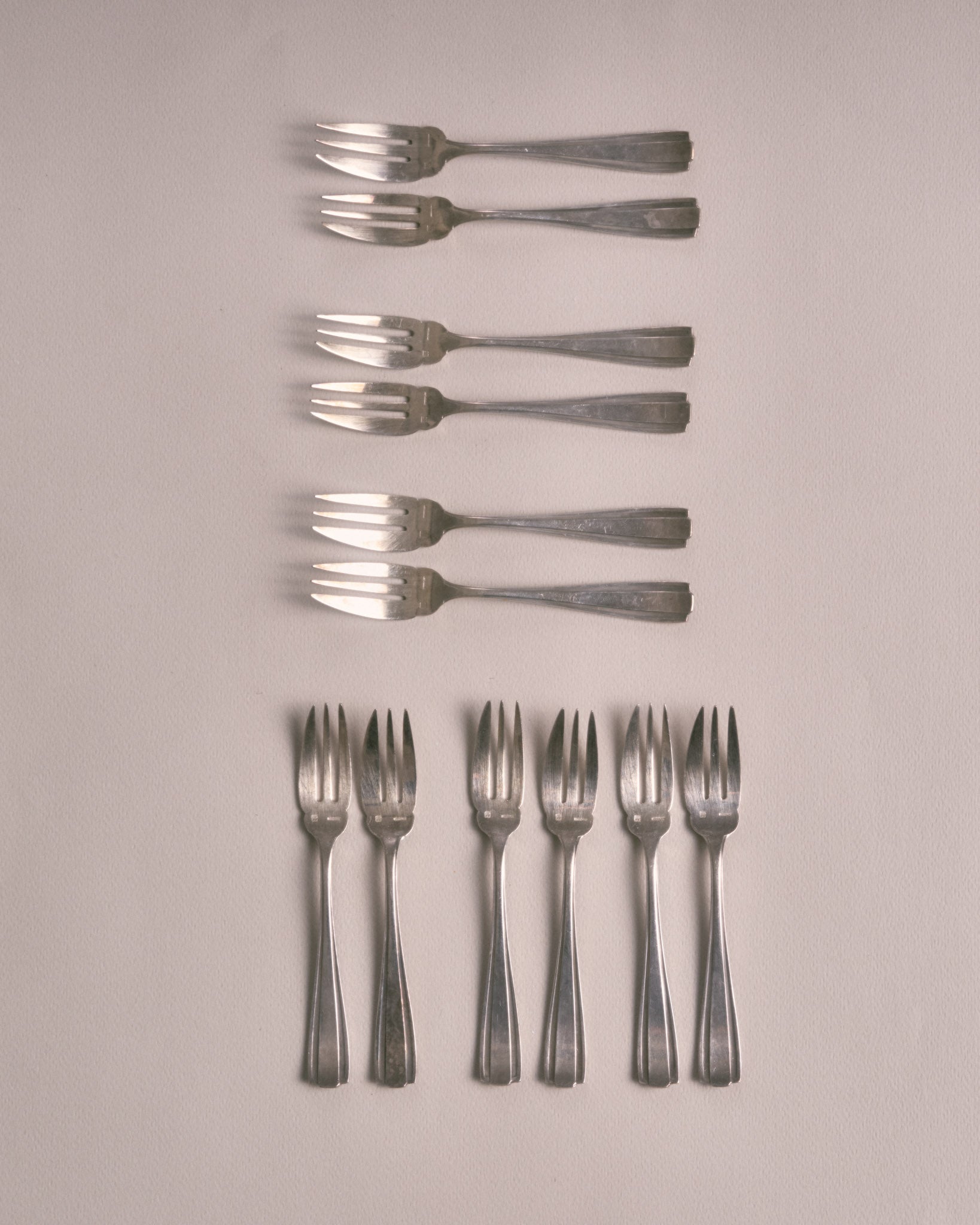 Service de 12 petites fourchettes à dessert en métal argenté dans leur écrin. Poinçonnées sur le devant. Design Art Déco. Très bon état, avec une patine conforme à l'âge et à l'usage. L'écrin est dans un bel état vintage.