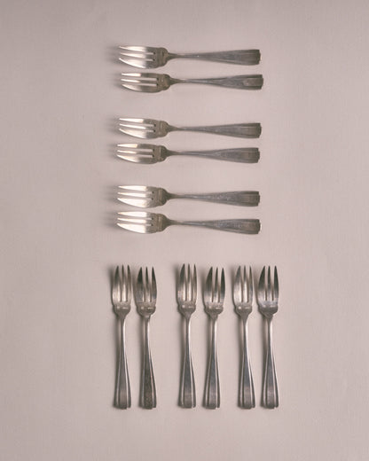 Service de 12 petites fourchettes à dessert en métal argenté dans leur écrin. Poinçonnées sur le devant. Design Art Déco. Très bon état, avec une patine conforme à l'âge et à l'usage. L'écrin est dans un bel état vintage.