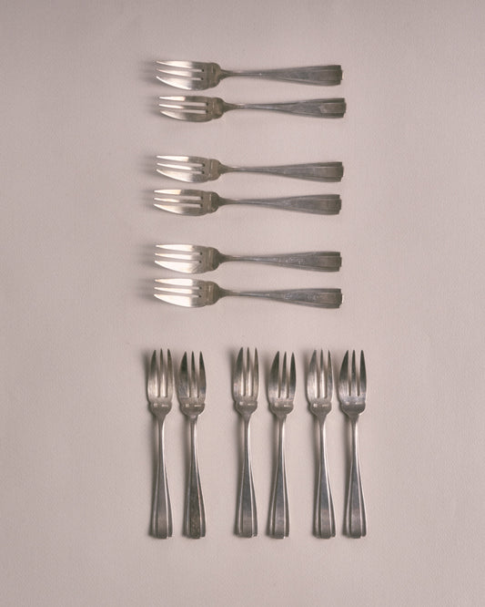 Service de 12 petites fourchettes à dessert en métal argenté dans leur écrin. Poinçonnées sur le devant. Design Art Déco. Très bon état, avec une patine conforme à l'âge et à l'usage. L'écrin est dans un bel état vintage.