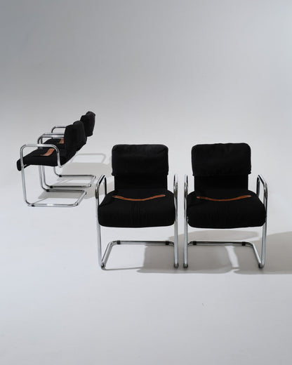 Set de 4 chaises de Guido Faleschini pour Mariani dans les années 1970. Structure en acier tubulaire chromé, assise et dossier généreusement rembourrés et recouverts d'un velours noir profond. Une sangle en cuir cognac, fixée par oeillets métalliques, souligne la ligne du siège.
