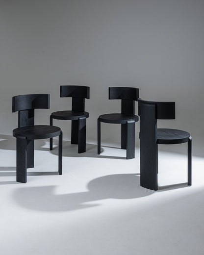 Set de 4 chaises "Spina" en chêne massif, finition teintée noir, par Louise Roe.&nbsp;
La collection Spina se caractérise par sa structure tripode et son assise circulaire. La pièce centrale, plus large, évoque la colonne vertébrale (spina en latin) et rappelle l’importance d’une posture droite.
Pensée pour la vie de tous les jours et en parfaite harmonie avec les tables "Pillabout", la chaise "Spina" arbore un arrière-dos cintré qui enveloppe l’usager et invite à la détente, alliant esthétique sculpturale 