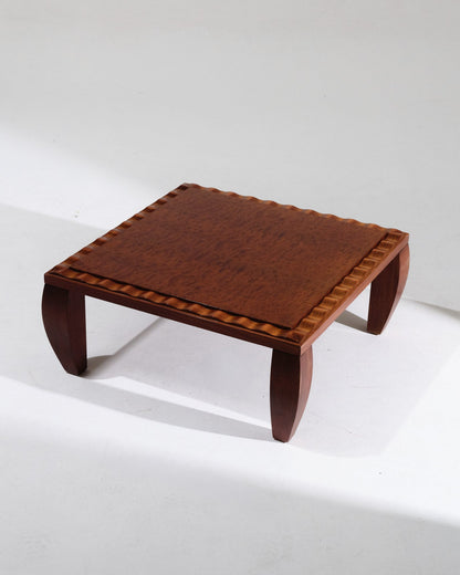 Table basse en bois bois de loupe vernis présentant un plateau à décor de bordure sculptée en vague, typique de l'esthétique Art Déco tardive. Parfait état