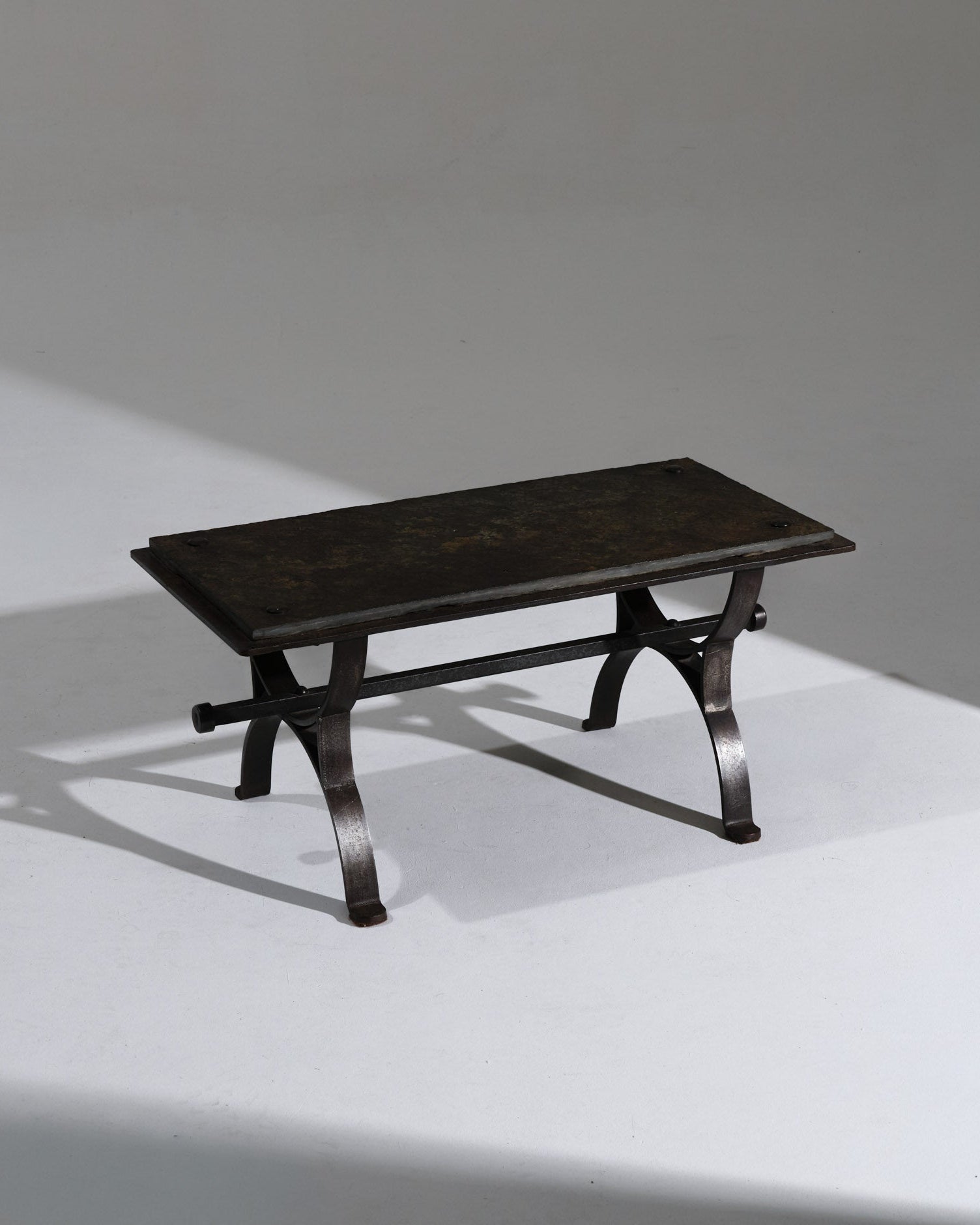 Table basse rectangulaire au piètement en fer forgé patiné, surmontée d'un plateau en ardoise naturelle aux nuances profondes. Les détails rivetés et la structure galbée confèrent à l'ensemble un caractère artisanal, typique du travail du fer français des années 1950. Très bel état.