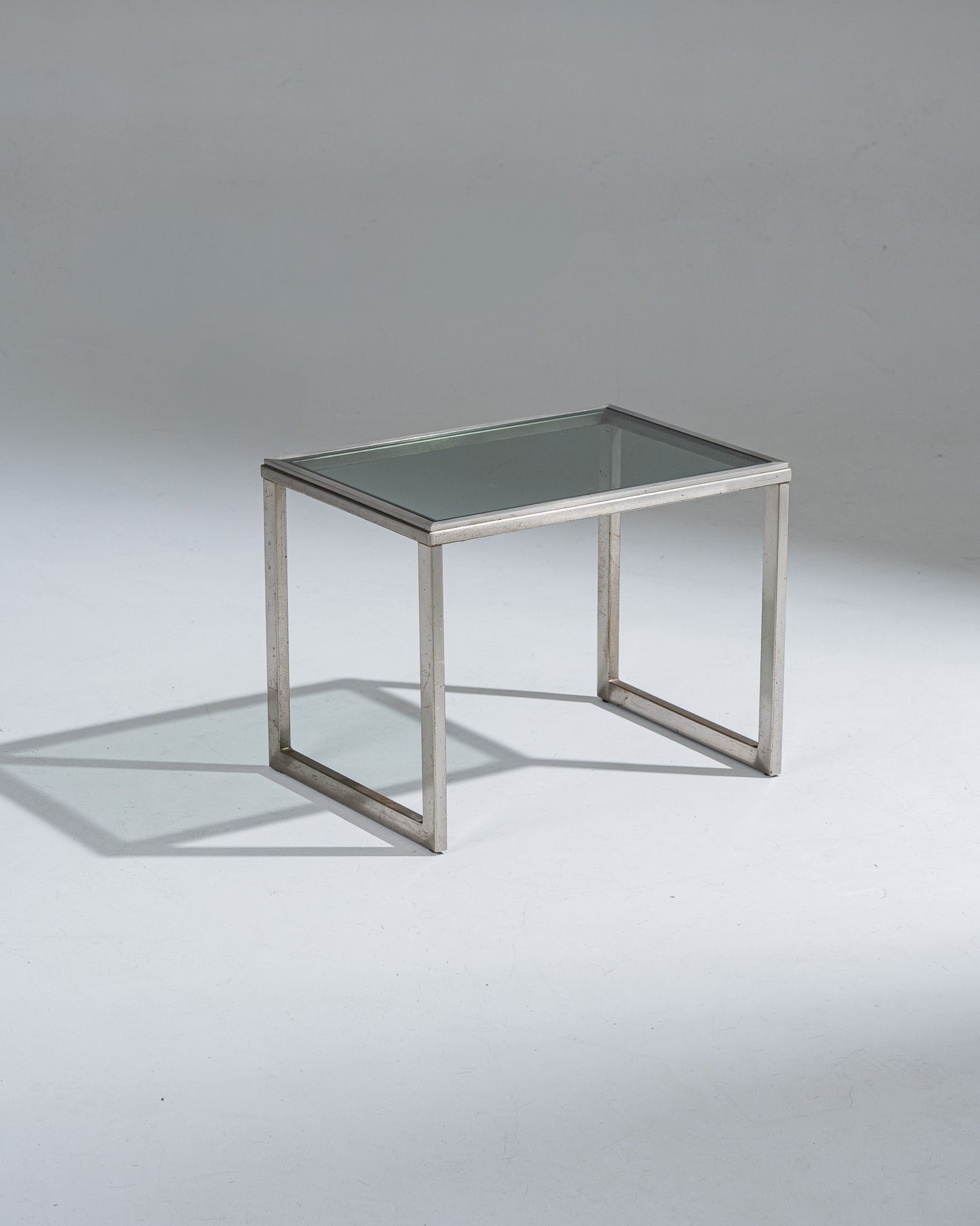 Petite table d'appoint rectangulaire en acier brossé et plateau en verre fumé. Patine sur l'acier et marque d'usure.