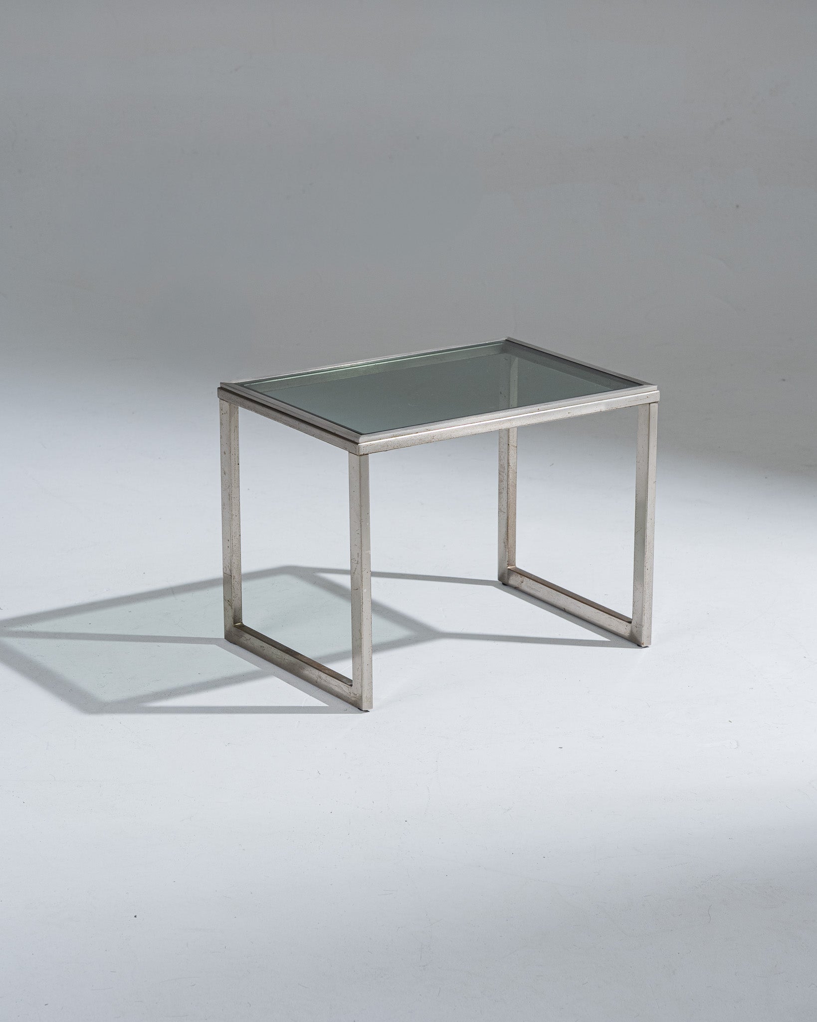 Petite table d'appoint rectangulaire en acier brossé et plateau en verre fumé. Patine sur l'acier et marque d'usure.