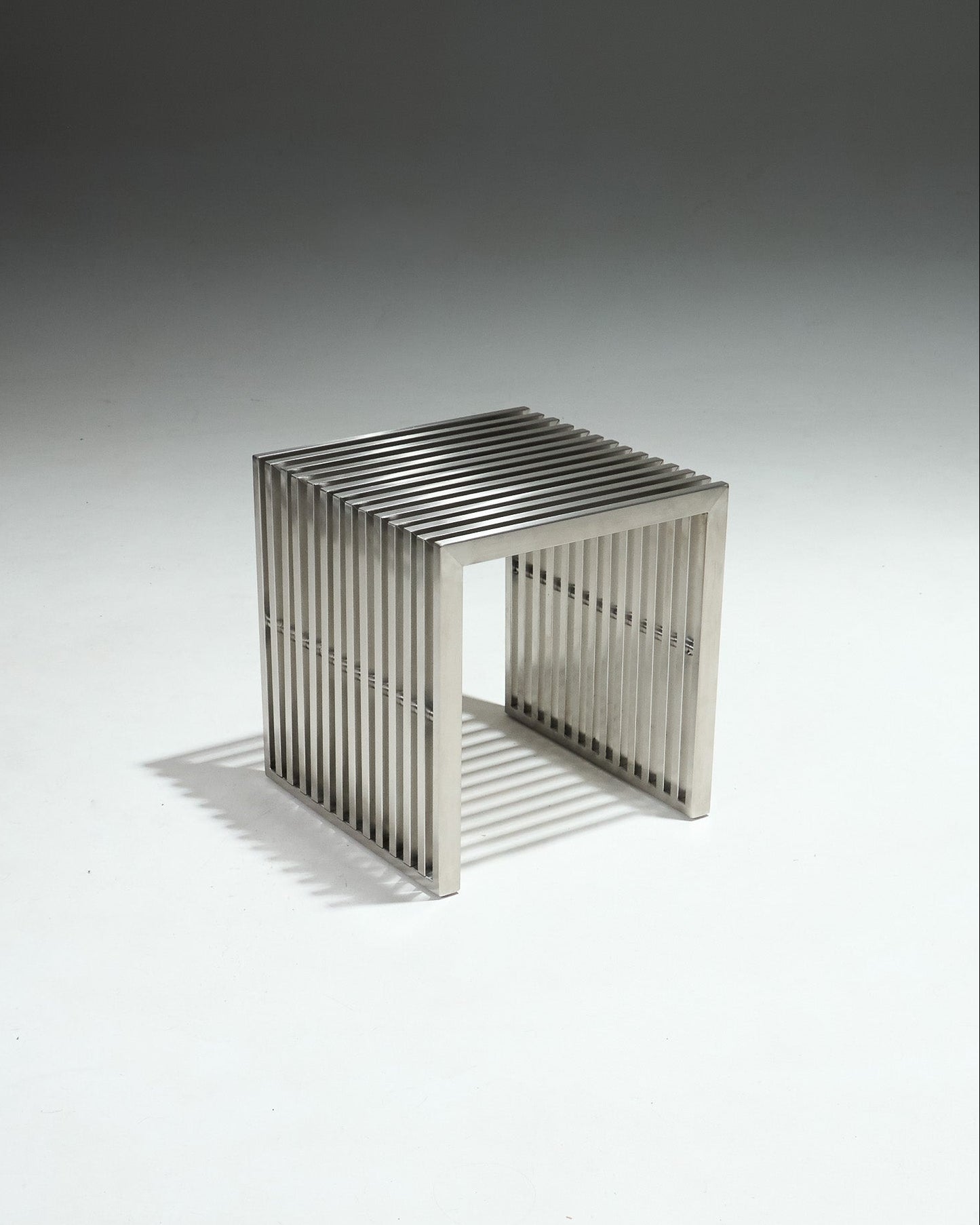 Tabouret moderniste en inox brossé, avec structure ajourée composée de lames verticales.&nbsp;Pièce dans l’esthétique minimaliste des années 1980, influencée par le design Bauhaus, mettant en avant des formes épurées et l’usage de matériaux industriels.&nbsp;