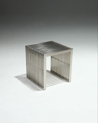 Tabouret moderniste en inox brossé, avec structure ajourée composée de lames verticales.&nbsp;Pièce dans l’esthétique minimaliste des années 1980, influencée par le design Bauhaus, mettant en avant des formes épurées et l’usage de matériaux industriels.&nbsp;