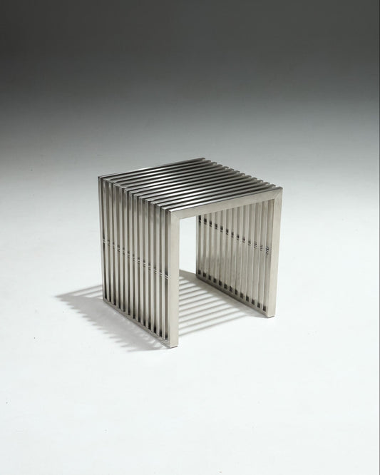 Tabouret moderniste en inox brossé, avec structure ajourée composée de lames verticales.&nbsp;Pièce dans l’esthétique minimaliste des années 1980, influencée par le design Bauhaus, mettant en avant des formes épurées et l’usage de matériaux industriels.&nbsp;