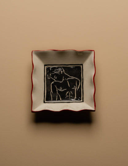 Petit vide-poche carré en céramique émaillée blanche à décor gravé d'un visage masculin entouré de motifs floraux. Pièce unique signée « Eldarov. T » au revers. Contour ondulé souligné d'un liseré rouge. Travail artisanal européen. Parfait état.