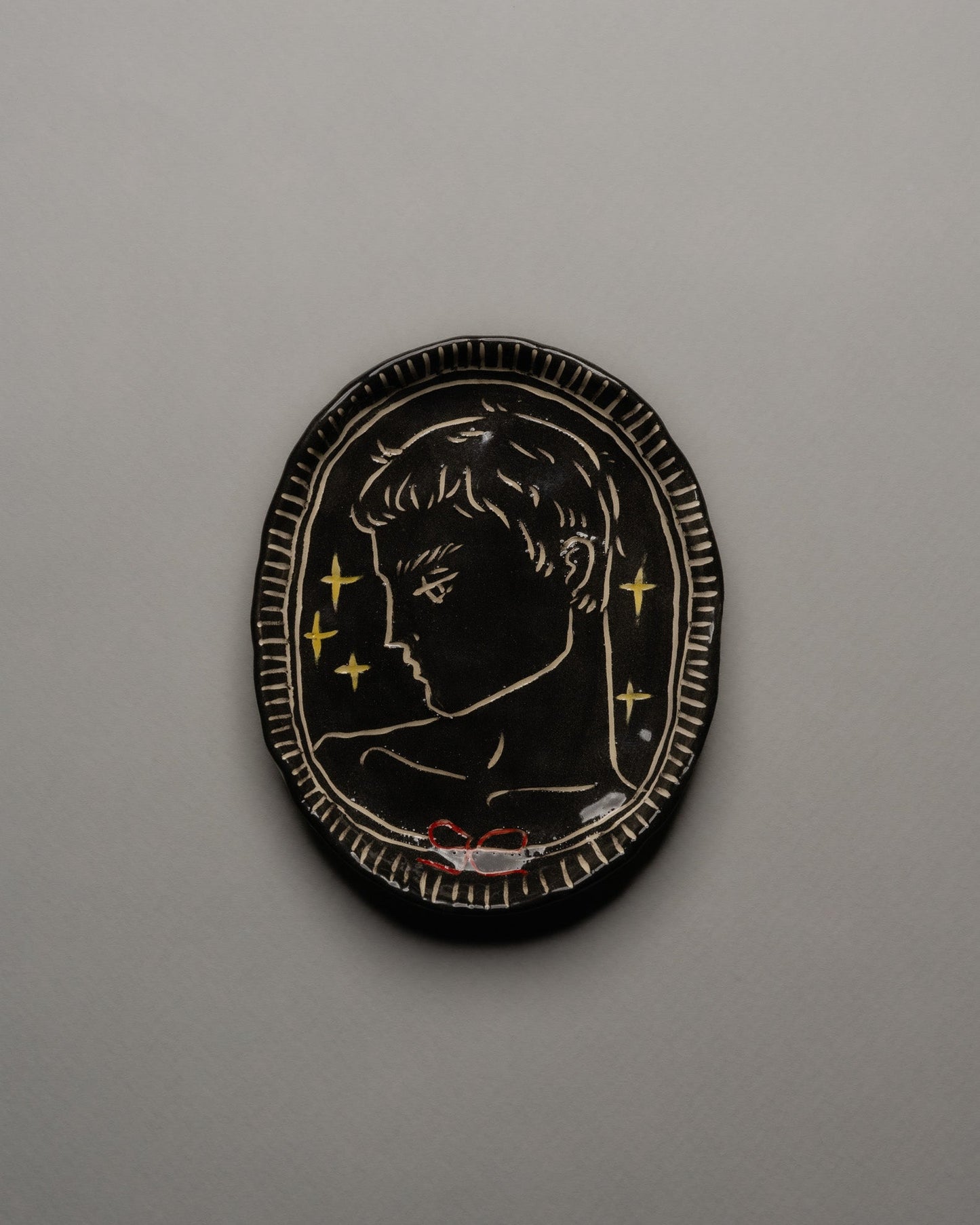 Vide-poche ovale en céramique émaillée noire, décor incisé d'un profil masculin orné d'étoiles dorées et d'un ruban rouge. Contour finement strié à la main. Pièce unique signée « Eldarov. T » au revers. Parfait état.