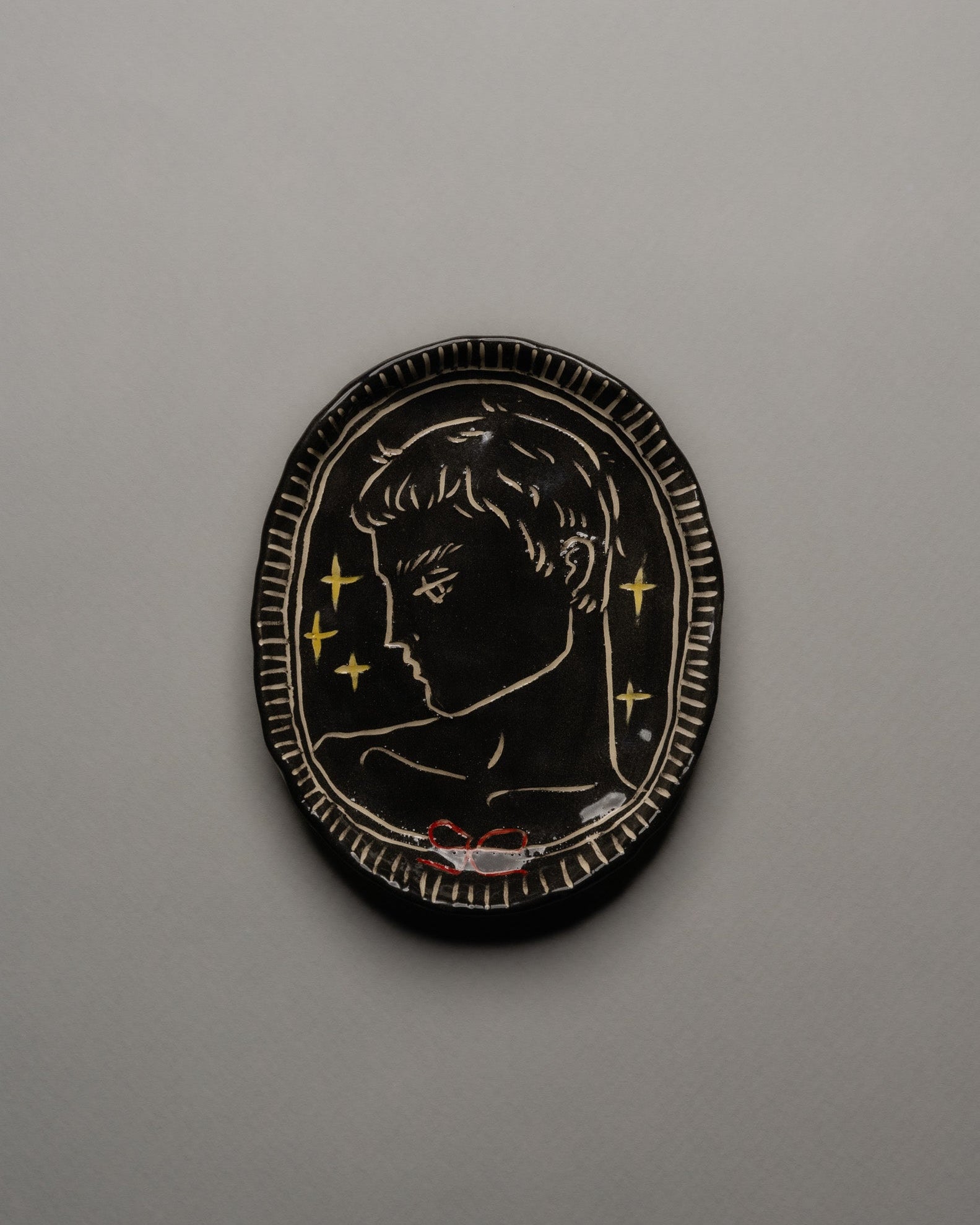 Vide-poche ovale en céramique émaillée noire, décor incisé d'un profil masculin orné d'étoiles dorées et d'un ruban rouge. Contour finement strié à la main. Pièce unique signée « Eldarov. T » au revers. Parfait état.