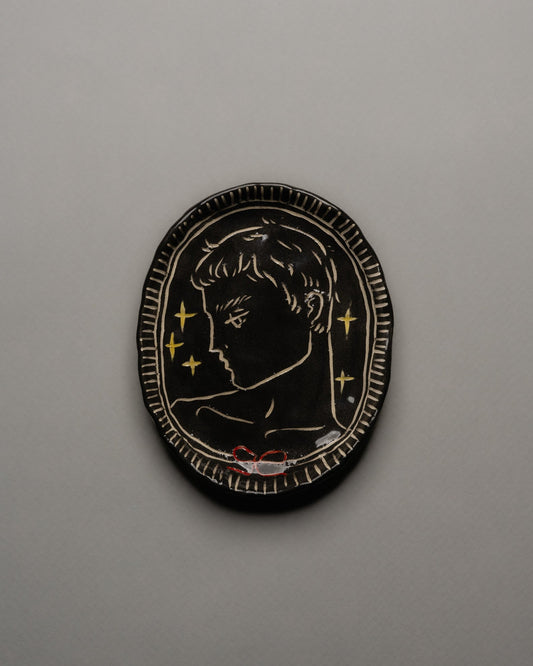 Vide-poche ovale en céramique émaillée noire, décor incisé d'un profil masculin orné d'étoiles dorées et d'un ruban rouge. Contour finement strié à la main. Pièce unique signée « Eldarov. T » au revers. Parfait état.