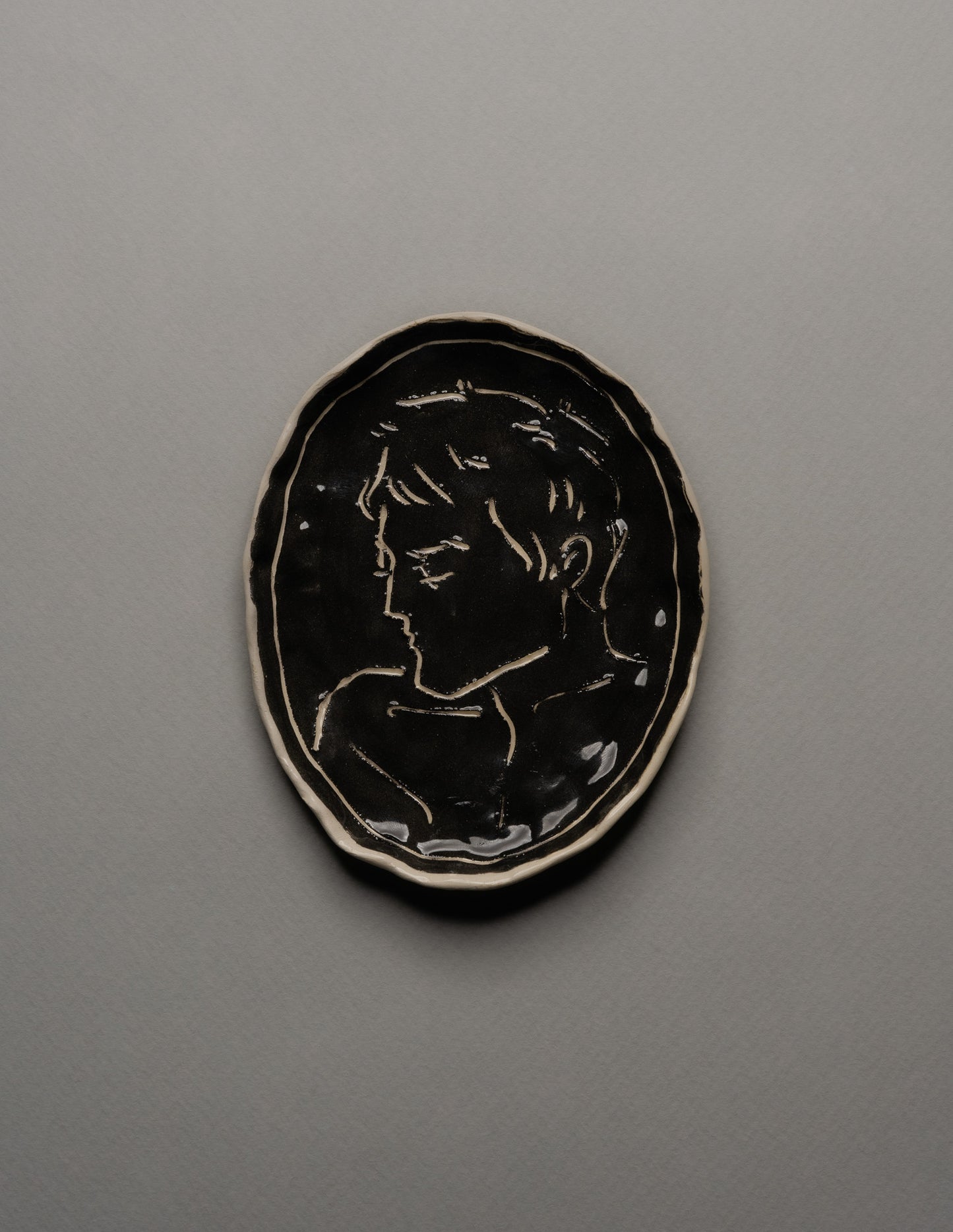 Vide-poche ovale en céramique émaillée noire, décor incisé d'un profil masculin stylisé sur fond brillant. Bord irrégulier souligné d'un fin filet blanc. Pièce unique signée « Eldarov. T » au revers. Parfait état.