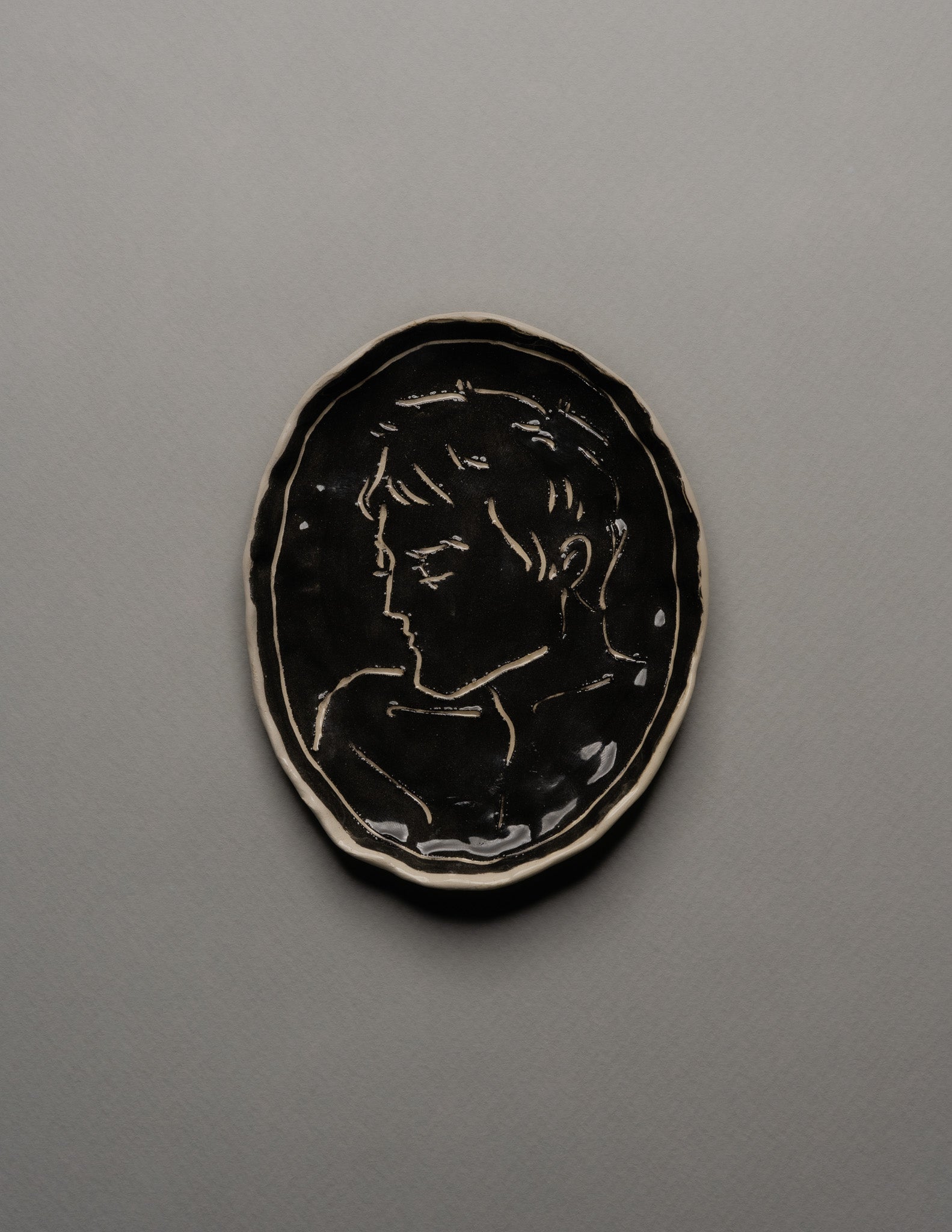 Vide-poche ovale en céramique émaillée noire, décor incisé d'un profil masculin stylisé sur fond brillant. Bord irrégulier souligné d'un fin filet blanc. Pièce unique signée « Eldarov. T » au revers. Parfait état.