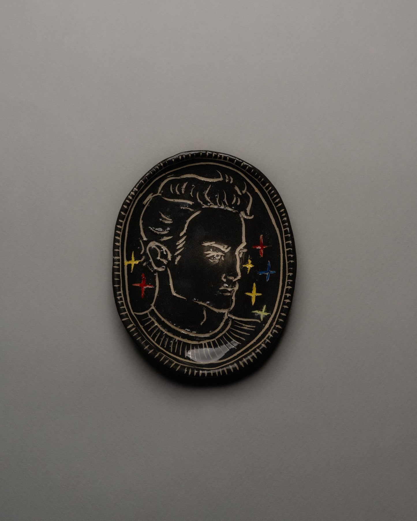 Vide-poche ovale en céramique émaillée noire, décor incisé d'un profil masculin orné d'étoiles colorées et d'un ruban rouge. Contour finement strié à la main. Pièce unique signée « Eldarov. T » au revers. Parfait état.
