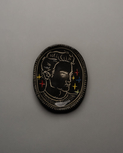 Vide-poche ovale en céramique émaillée noire, décor incisé d'un profil masculin orné d'étoiles colorées et d'un ruban rouge. Contour finement strié à la main. Pièce unique signée « Eldarov. T » au revers. Parfait état.