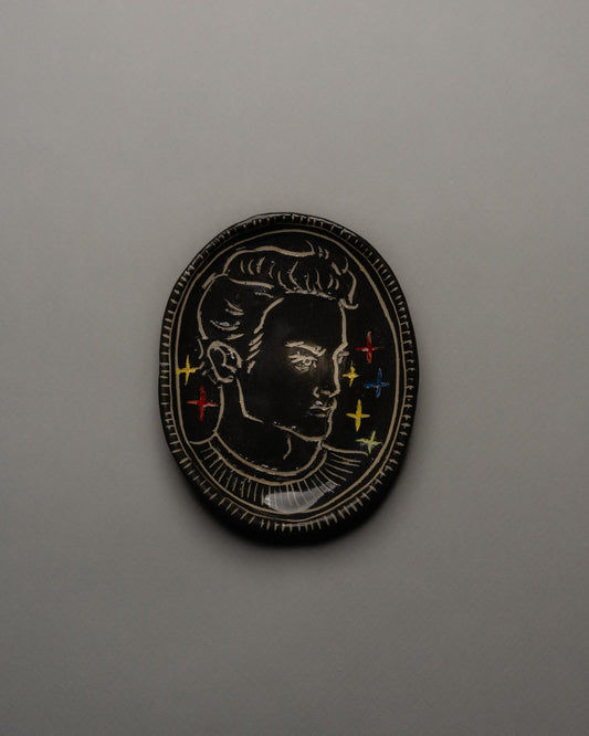 Vide-poche ovale en céramique émaillée noire, décor incisé d'un profil masculin orné d'étoiles colorées et d'un ruban rouge. Contour finement strié à la main. Pièce unique signée « Eldarov. T » au revers. Parfait état.