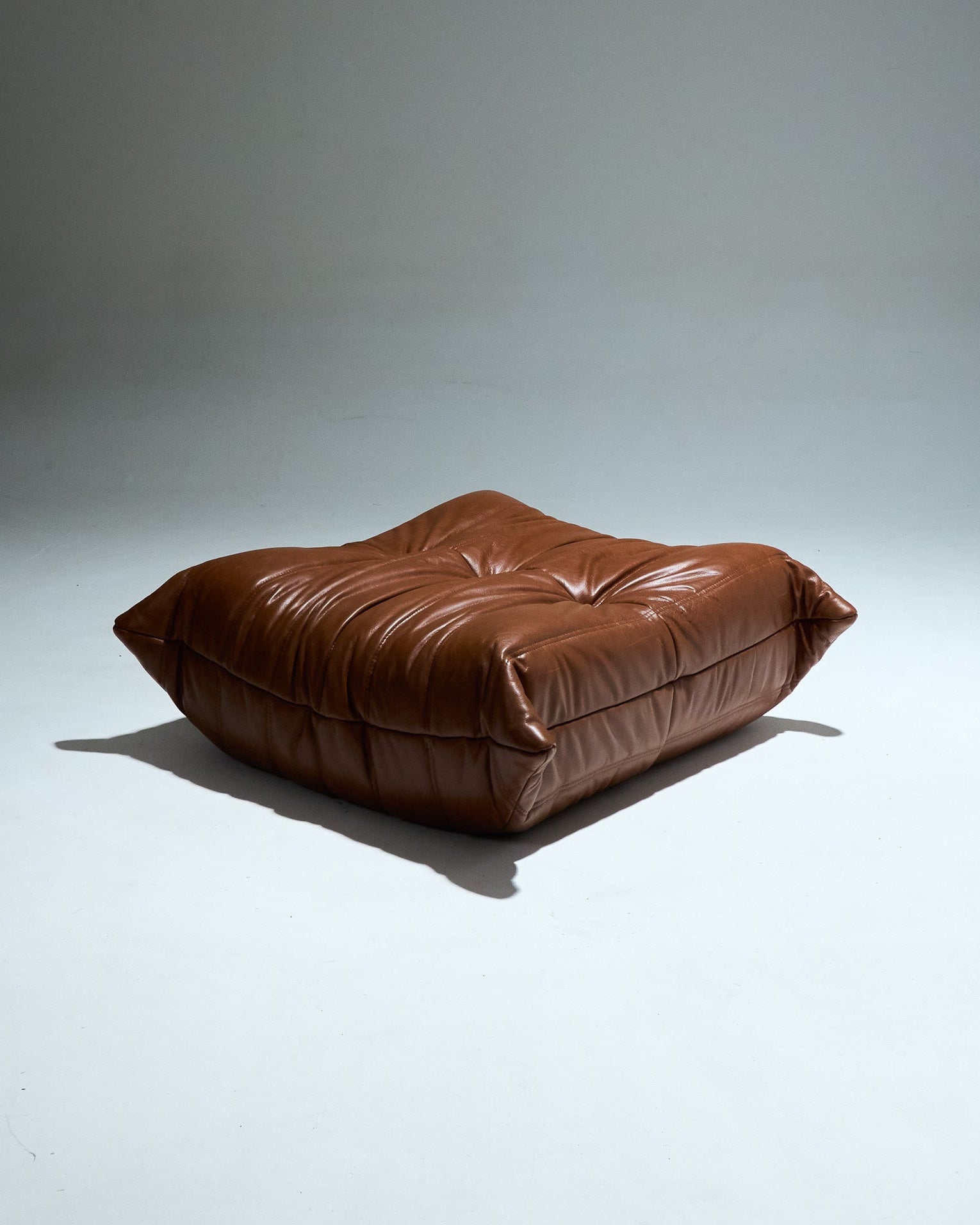 Ottoman TOGO du designer Michel Ducaroy (1925-2009) pour Ligne Roset dans les années 1970. Grand classique du design cet ottoman entièrement en mousse est recouvert d'une housse en cuir brun d'origine. Pièce étiquetée.
Très bon état général. À noter, une légère décoloration du cuir à certains endroits (voir photo).&nbsp;&nbsp;